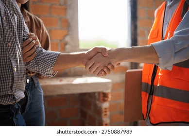 Two people shaking hands, one wearing an orange safety vest and holding a clipboard, possibly at a construction site. Another person stands nearby. A brick wall and window are in the background, highlighting Building Services Sydney in action.
